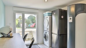 A compact kitchen with a washing machine, a refrigerator, and a dining area with chairs. - Grande Maison avec Jardin, Parking, proche de la Plage (Les Sables-d'Olonne)
