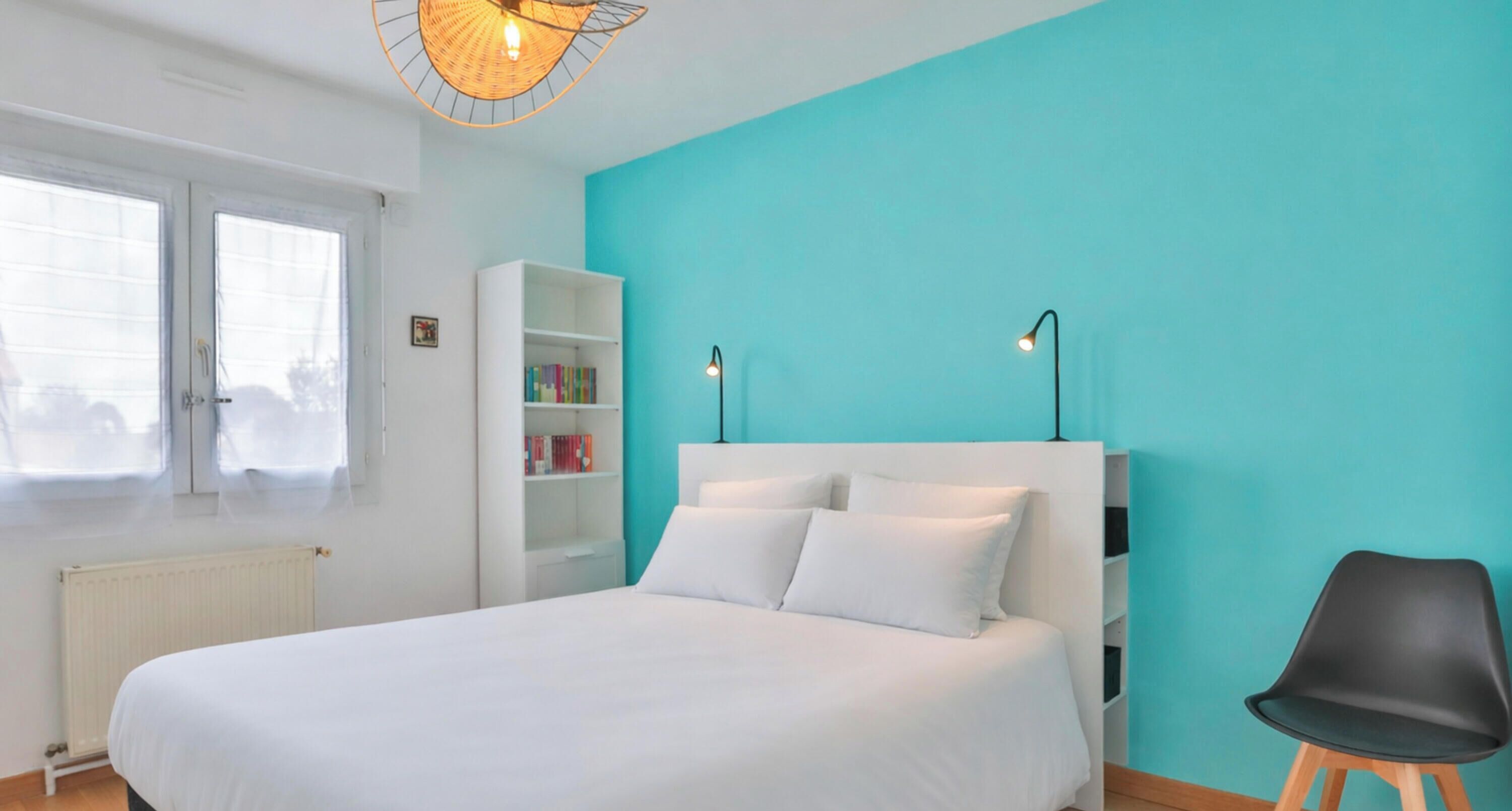 A bedroom with a bed, a white bookshelf, a black chair, and a teal wall.