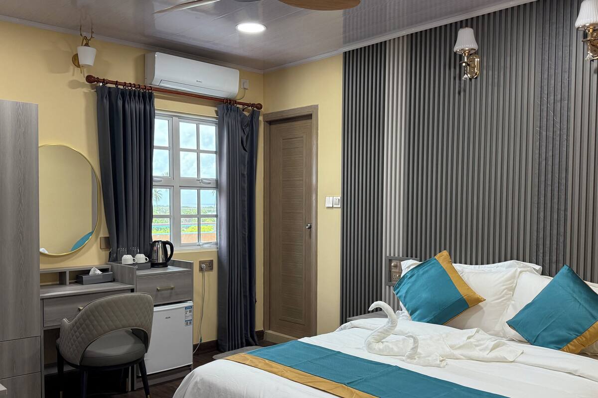 Habitación de hotel con cama, escritorio, silla, espejo y ventana con cortinas.
