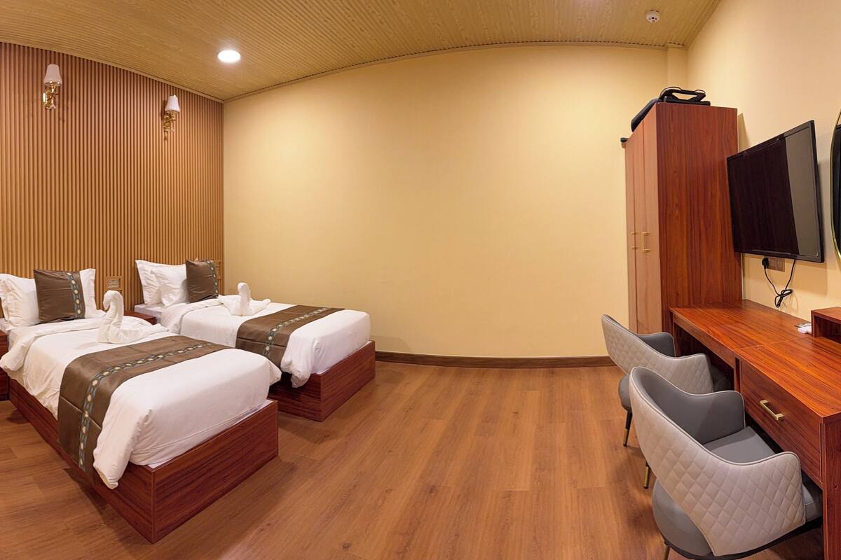 Una habitación de hotel con dos camas, un escritorio, una silla, un espejo y un televisor.