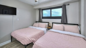 A bedroom with two beds, a ceiling fan, a window with curtains, and a mounted TV.