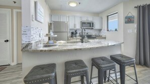 A kitchen with a marble countertop, stainless steel appliances, and three bar stools.