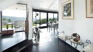 Ein modernes Interieur mit Essbereich, einer kleinen Sitzecke und einem großen Fenster mit Blick ins Freie.