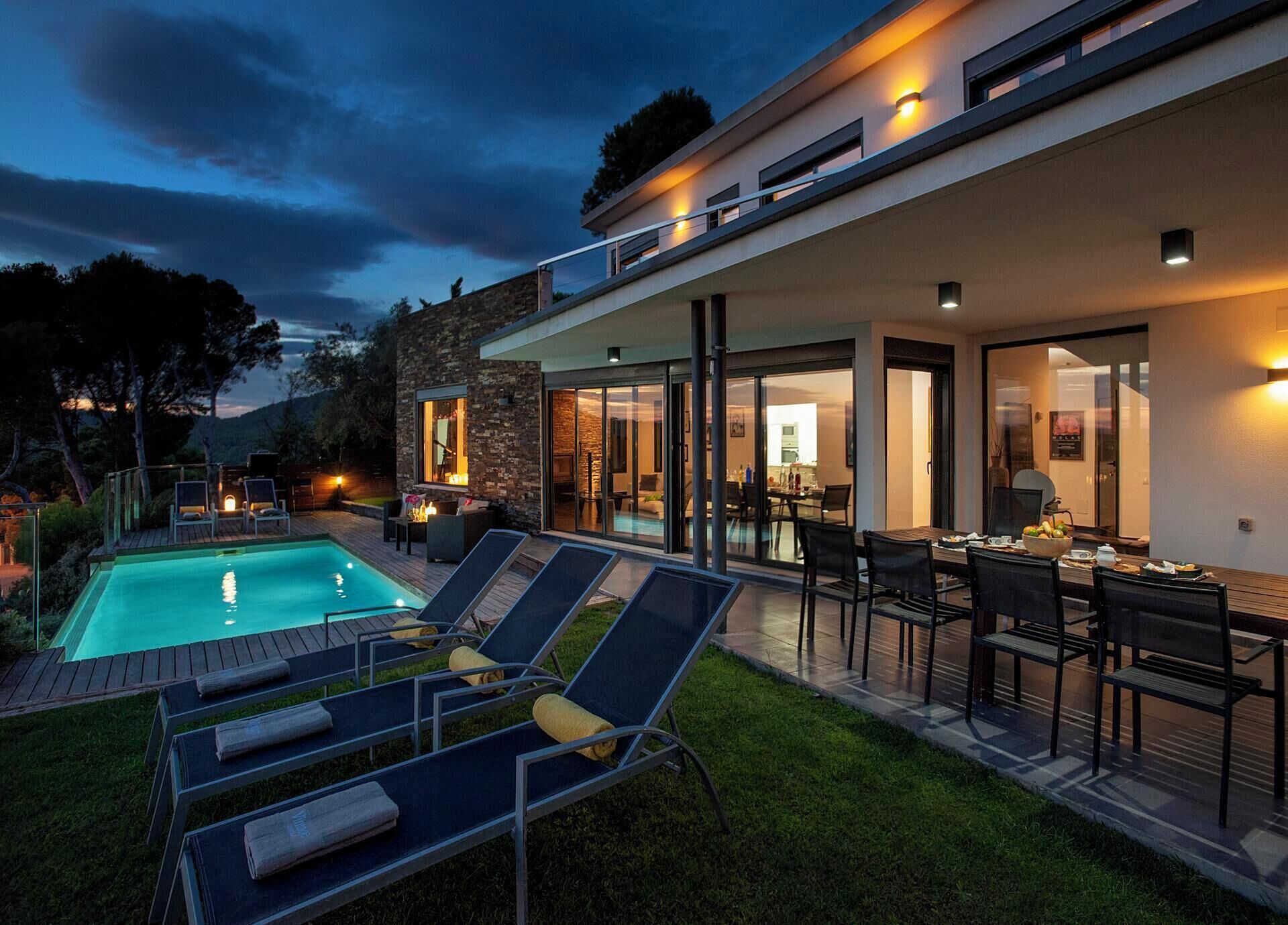 A modern house with a swimming pool, outdoor seating, and a dining area.