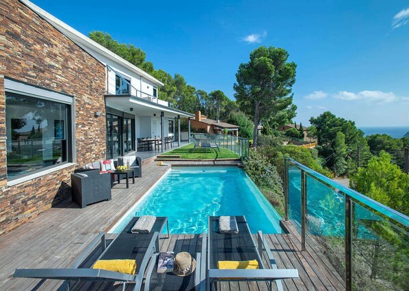 Uma casa moderna com piscina, móveis de exterior e vista para o mar.