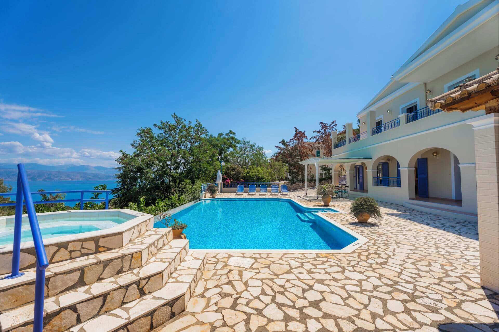 A pool area with stone steps leading to a pool, a pergola, and a view of the sea.