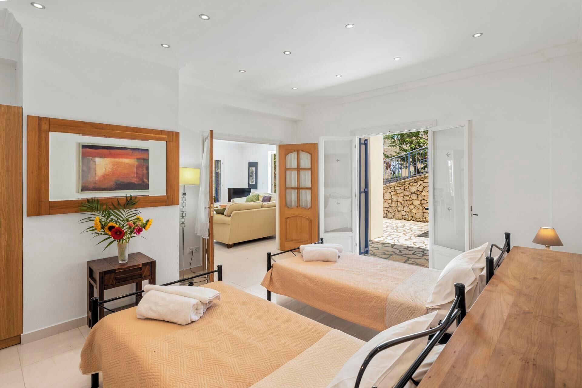 Habitación de hotel con dos camas, un cuadro, un jarrón con flores y vistas al exterior.