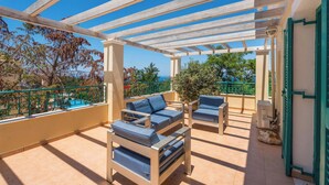 Ein überdachter Außenbereich mit zwei Sofas und einem Tisch, mit Blick auf einen Pool und Bäume.