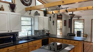 Una cocina con armarios de madera, encimera negra, estufa empotrada y ventana con persianas.
