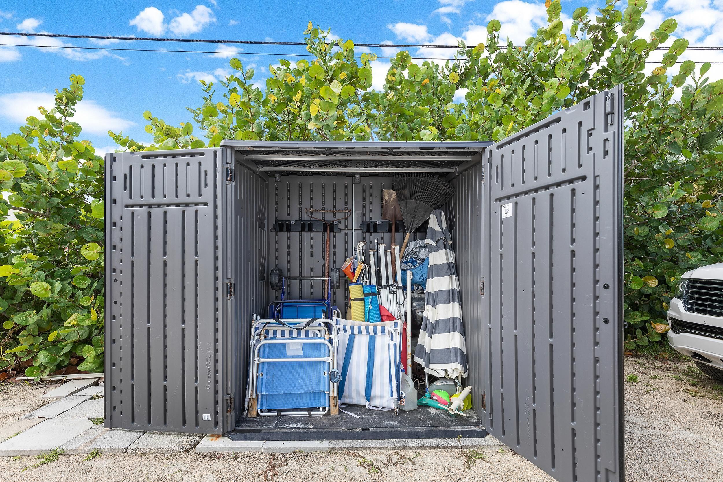 Un mueble metálico compacto con la puerta abierta, mostrando una maleta azul y una bolsa a rayas en su interior.