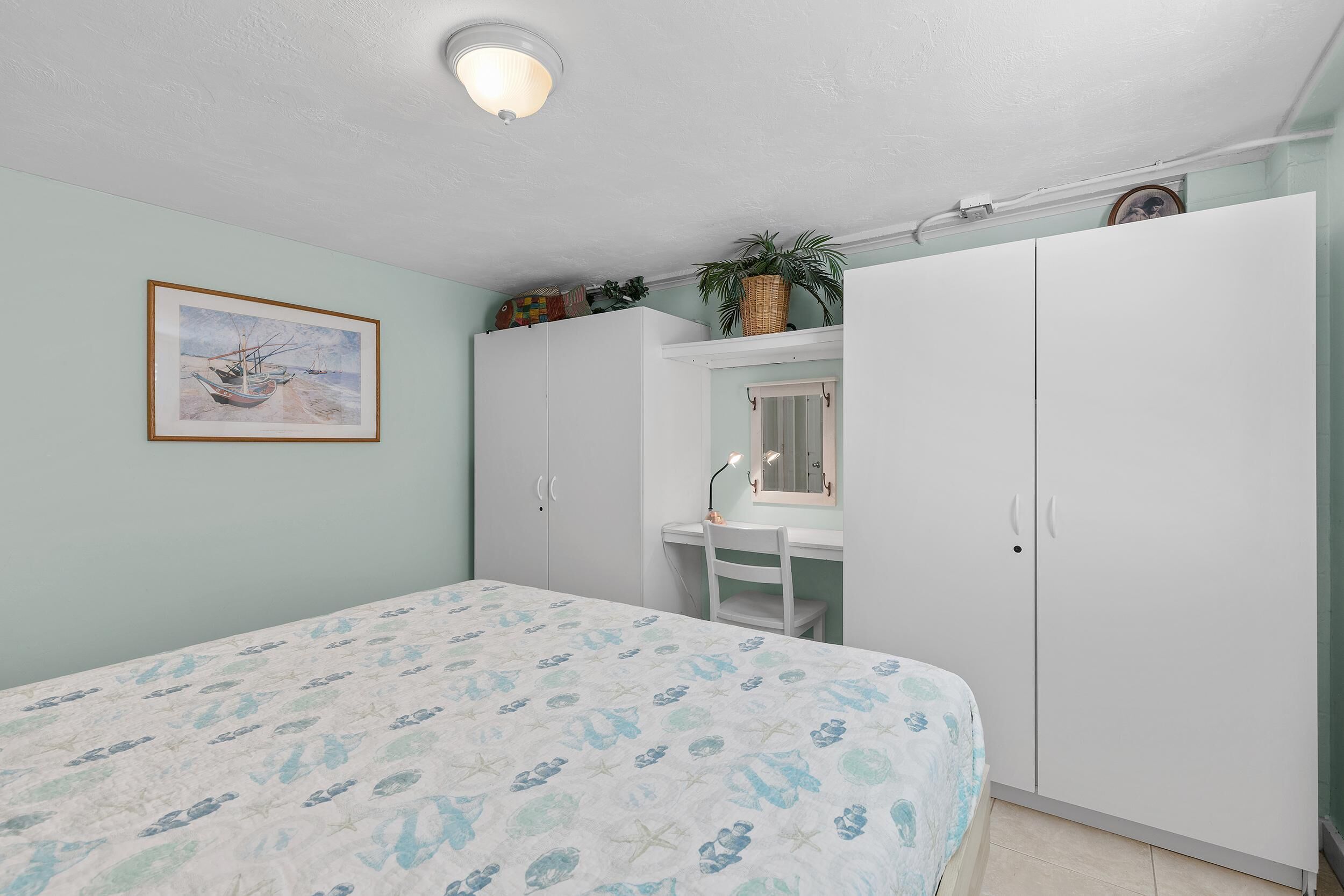 A bedroom with a bed, a desk, a wardrobe, and a framed picture on the wall.