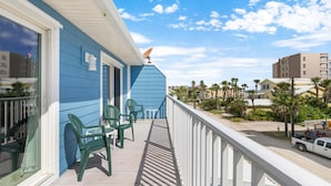 A balcony with green chairs, a white railing, and a view of a beach and buildings.