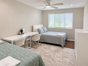 A bedroom with a bed, a desk, a chair, a radiator, a window with blinds, and a ceiling fan. - Modern 3-bed Hub resort / ping pong & pool table. Game room (San Diego)