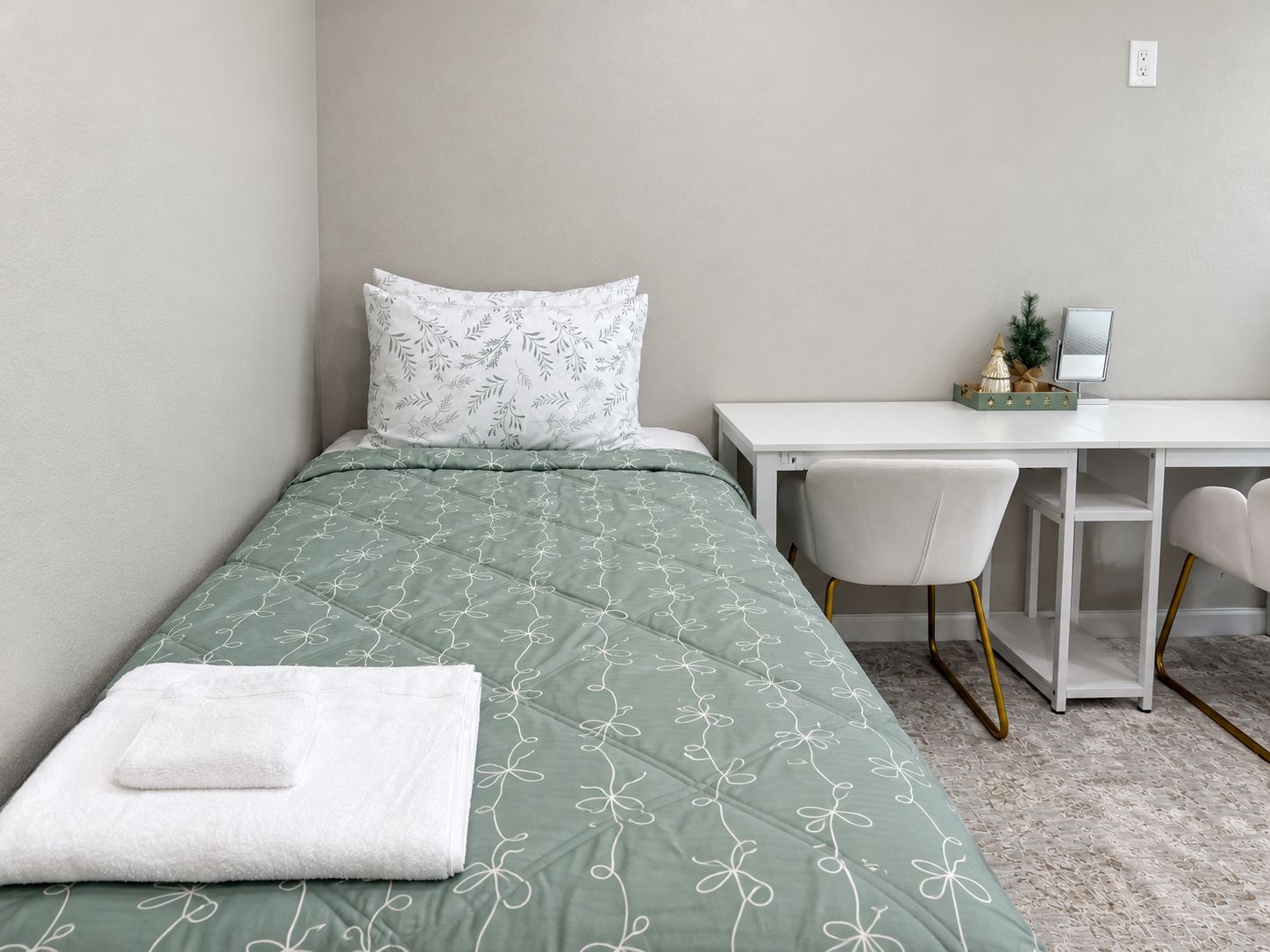 Un lit simple avec une couvre-lit à motifs floraux verts, un oreiller blanc et une serviette blanche sur le lit.