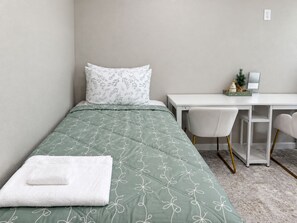 A single bed with a green floral bedspread, a white pillow, and a white towel on the bed. - Modern 3-bed Hub resort / ping pong & pool table. Game room (San Diego)