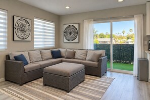 A modern living room with a sectional sofa, a coffee table, and a large window with a view of palm trees. - Modern 3-bed Hub resort / ping pong & pool table. Game room (San Diego)
