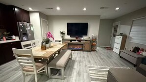 En moderne stue med pejs, et spiseområde med et træbord og stole, et fjernsyn ophængt på væggen og en sofa.