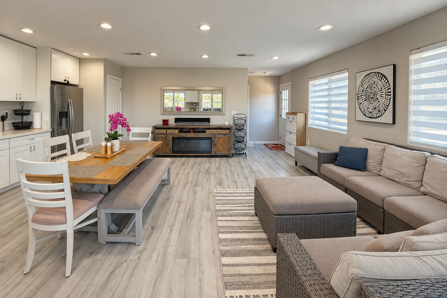A modern kitchen with a dining area, a sofa, and a large window with blinds.