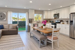 Una cocina moderna con armarios blancos, electrodomésticos de acero inoxidable y un comedor con mesa y sillas de madera.