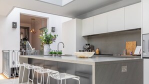 A modern kitchen with a central island, bar stools, a coffee machine, and a large window. - Eccleston Street III by onefinestay (London)
