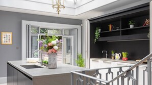 A modern kitchen with a central island, a built-in sink, and a black shelving unit with plants. - Eccleston Street III by onefinestay (London)