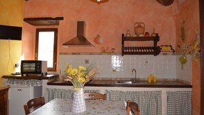A kitchen with a wooden ceiling, a microwave, a sink, and a dining table with a vase of flowers.