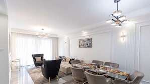 Een moderne eetruimte met een glazen tafel, comfortabele stoelen en een kroonluchter.