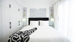 Een moderne hotelkamer met een groot bed, witte muren, een marmeren hoofdeinde en twee bedlampjes.