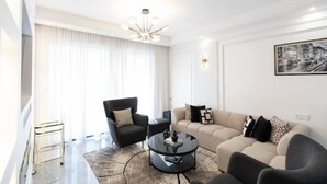 Een moderne woonkamer met een bank, fauteuils, een salontafel en een kroonluchter.