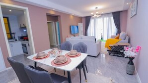 A modern living room with a dining area, a sofa, and a TV. - Lymack Suites, 1BR Fourways Junction , Kiambu Road (Nairobi)