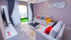 A modern living room with a grey sofa, a coffee table, and a TV on a stand. - Lymack Suites, 1BR Fourways Junction , Kiambu Road (Nairobi)