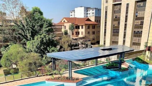 A swimming pool with a sunken area and a covered seating area, surrounded by greenery and buildings. - Lymack Suites, 1BR Fourways Junction , Kiambu Road (Nairobi)