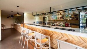 Een bar met een houten toog, witte barstoelen en schappen vol flessen.