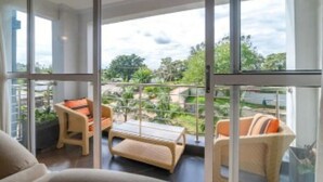 Een balkon met rieten meubilair, een glazen deur en uitzicht op groen.