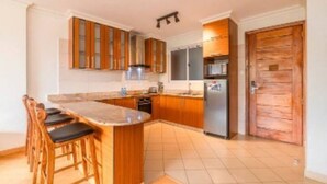 Een keuken met houten kastjes, een centraal eiland met barstoelen, een magnetron en een koelkast.