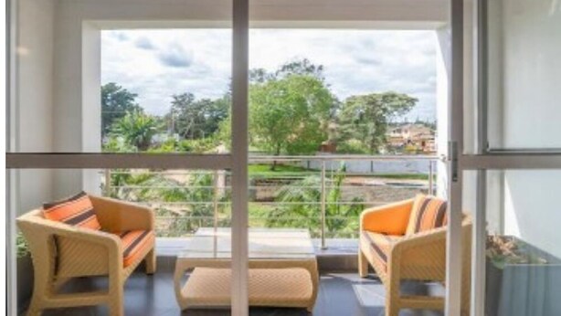 Een balkon met rieten meubilair en uitzicht op groen en gebouwen.