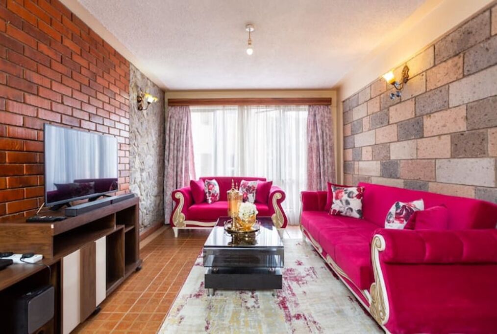 Ein Wohnzimmer mit Backsteinwand, einem roten Sofa, einem Couchtisch und einem Fernseher auf einem Holzboden.
