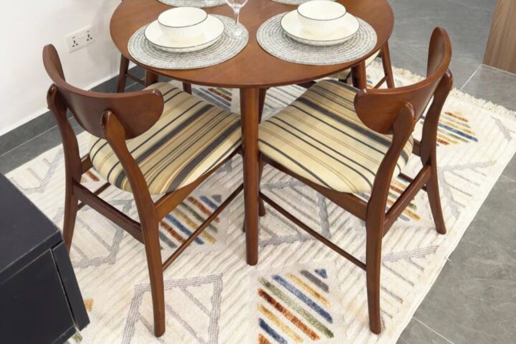A dining table with four chairs, each with a striped cushion. The table has a round wooden top and is set with white plates and a glass.