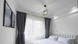 A bedroom with a white bed, grey curtains, and a single light fixture.