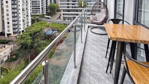A balcony with a view of a cityscape, a hanging chair, and a table with chairs.