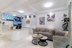 A modern reception area with a white reception desk, a grey sofa with patterned cushions, and a round coffee table. - Alba Garden, Modern / Infinity Pool/Gym & Minimart (Nairobi)