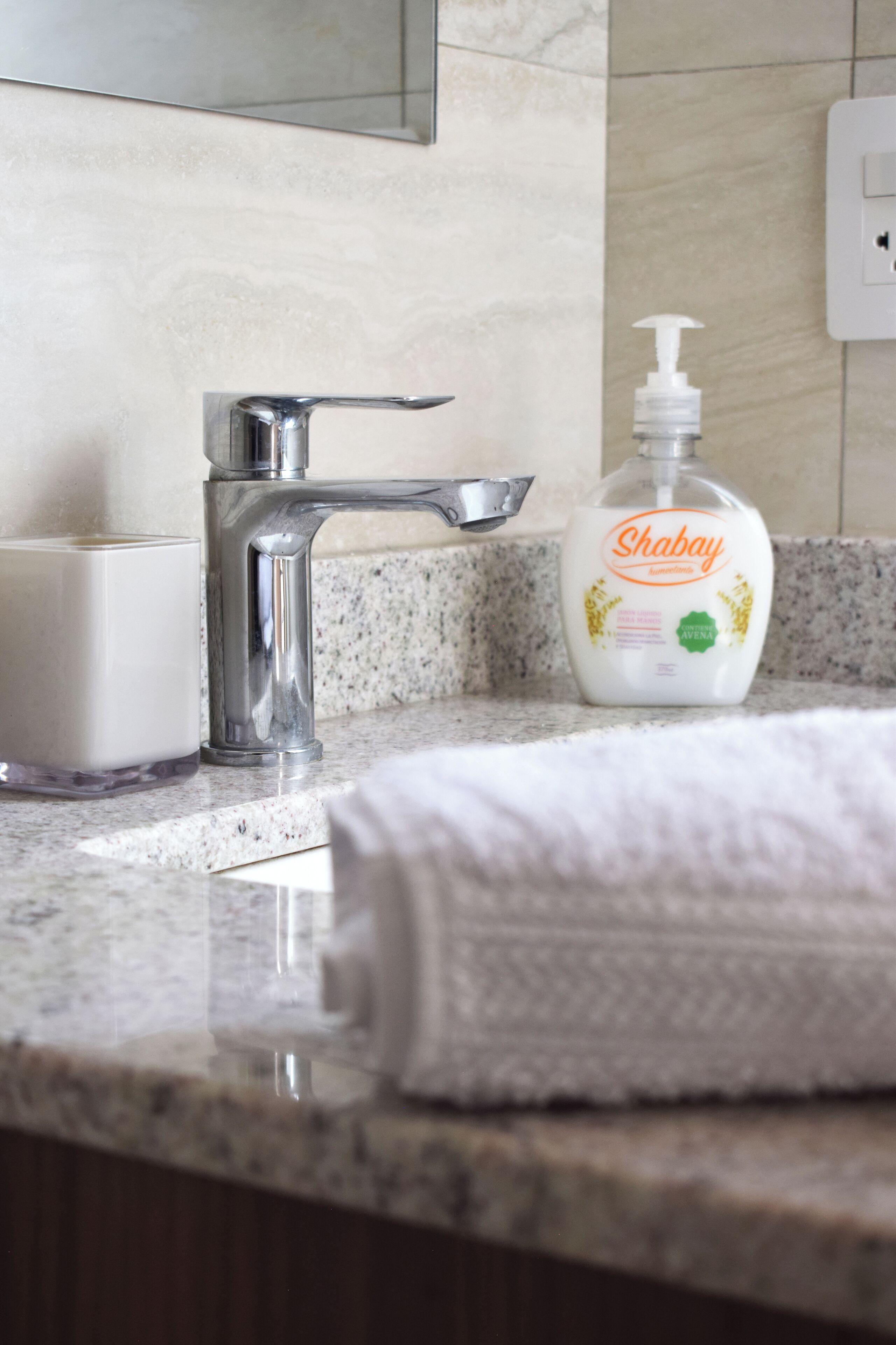 Un baño con encimera de mármol, dispensador de jabón blanco y una toalla.