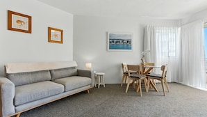 Een hotelkamer met een grijze bank, een eettafel met stoelen, een lamp en twee ingelijste foto's aan de muur.