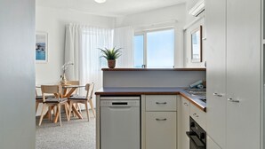 Een kleine keuken met een vaatwasser, oven en een raam met gordijnen. Er is een zithoek met een tafel en stoelen.