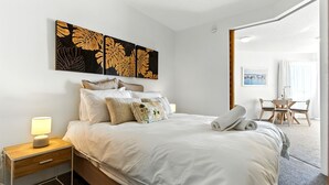 Een hotelkamer met een bed, kussens, een nachtkastje, een lamp en kunst aan de muur.