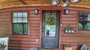 A wooden cabin with a front door, a welcome mat, a bench, and a small table.