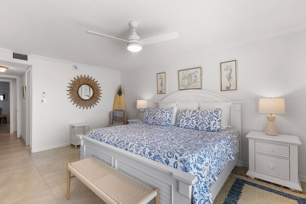 Une chambre à coucher comprenant un lit, des tables de chevet, un banc et un ventilateur de plafond.