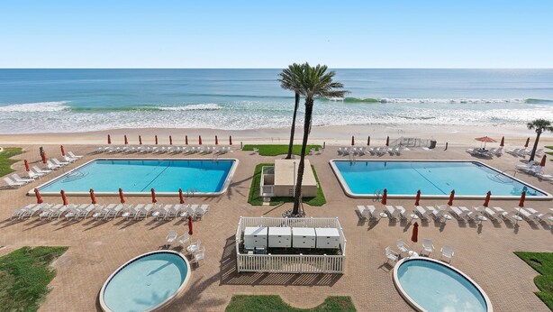 A resort pool area with two rectangular pools, a palm tree, and beach views. - Sandpiper 108 (New Smyrna Beach)