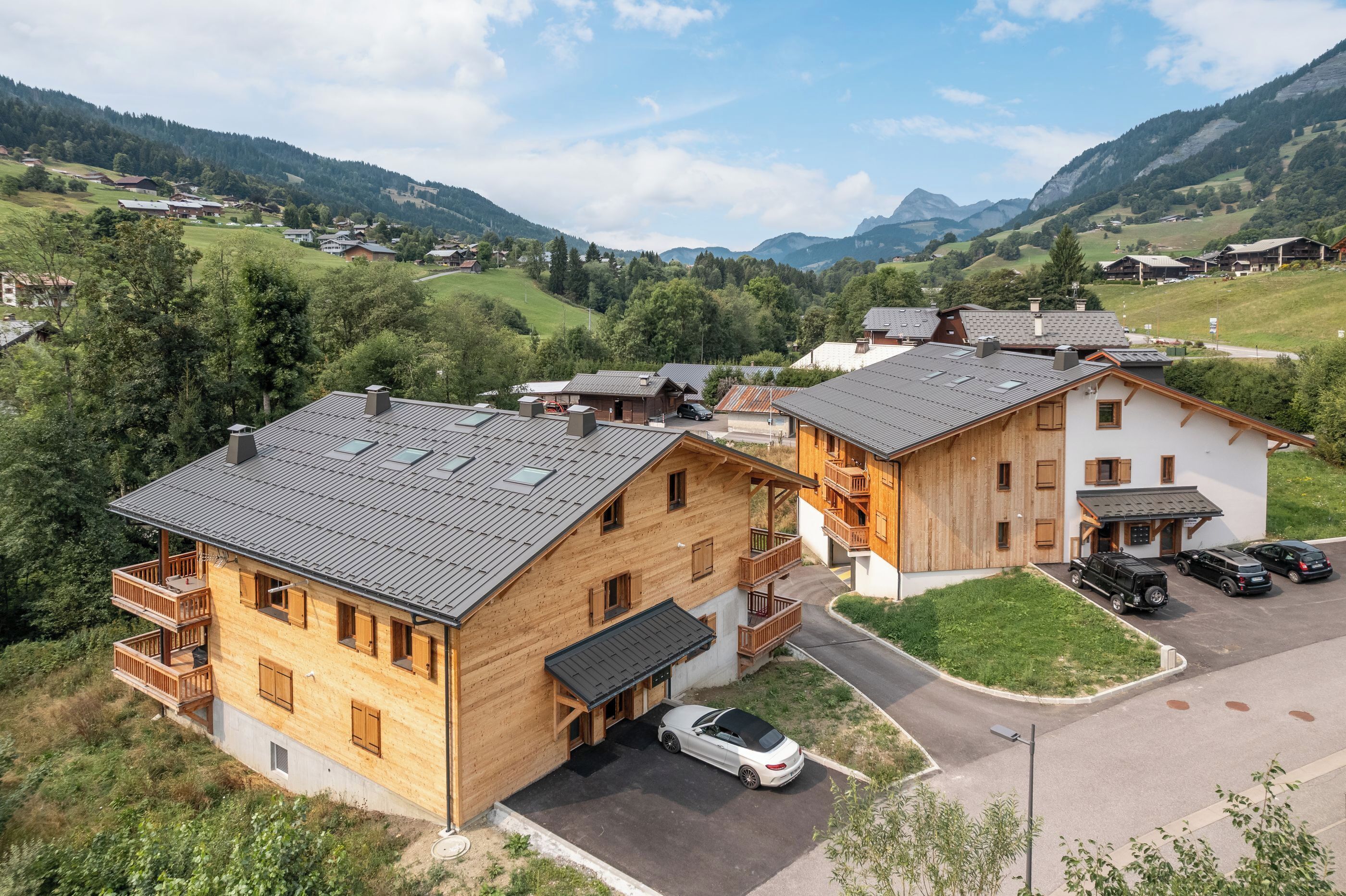 En stuga i trä med en balkong, ett carport och utsikt över ett bergigt landskap.
