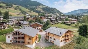 Eine Gruppe von Holzhäusern mit Balkonen, eingebettet in eine hügelige Landschaft unter blauem Himmel.